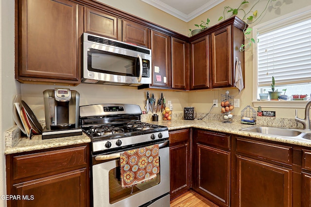 kitchen featuring appliances with stainless steel finishes, a sink, crown molding, light stone counters, and light wood-style flooring