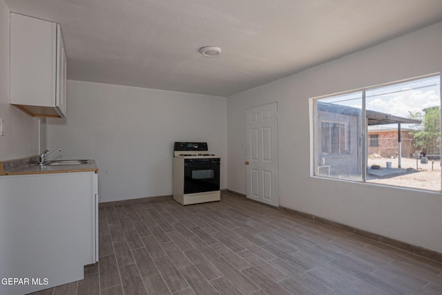 318 Austin St, Fabens, TX 79838 - kitchen with gas stove, a sink, white cabinets, baseboards, and wood finished floors