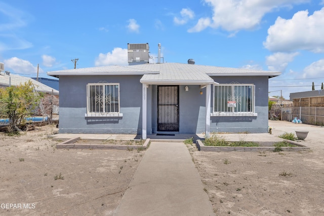 bungalow-style house with fence, stucco siding, and cooling unit