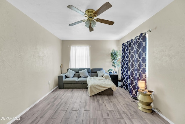 living area with wood finished floors, a ceiling fan, and baseboards