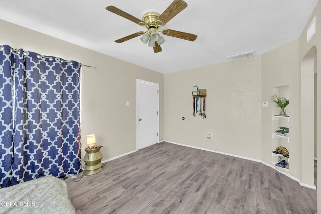 living room featuring wood finished floors, a ceiling fan, arched walkways, and baseboards
