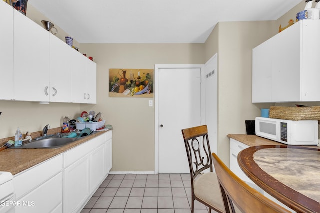 kitchen with white microwave, a sink, light tile patterned floors, and white cabinetry