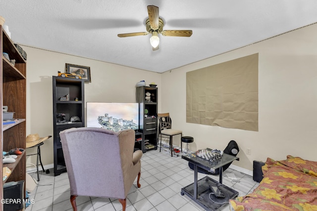 living area featuring a ceiling fan, a textured ceiling, light tile patterned flooring, and baseboards