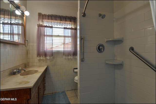 full bath with healthy amount of natural light, tile patterned floors, a tile shower, vanity, and tile walls