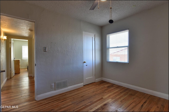 spare room with hardwood / wood-style flooring, plenty of natural light, a textured ceiling, and a ceiling fan