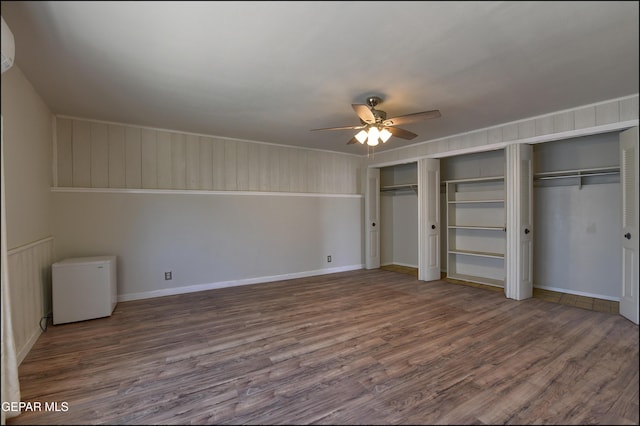 unfurnished bedroom featuring wood finished floors, refrigerator, two closets, a ceiling fan, and baseboards