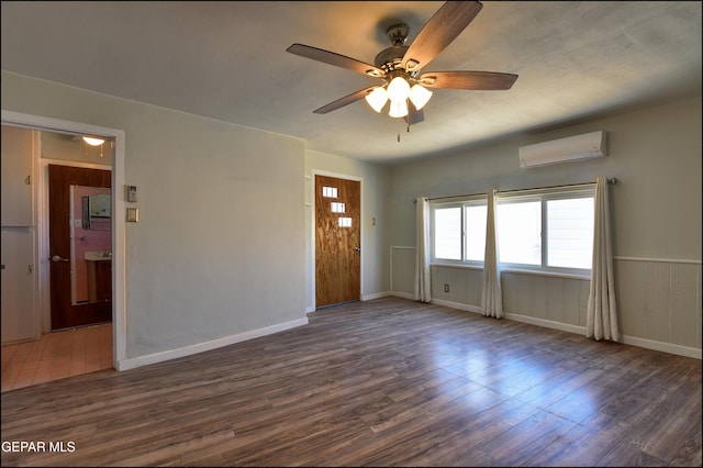 spare room featuring a wall unit AC, dark wood-style floors, a ceiling fan, and baseboards