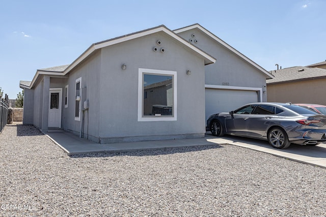 view of property exterior featuring a garage, driveway, stucco siding, and fence