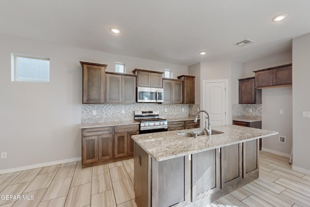 14813 Pebble Hills Blvd, El Paso, TX 79938 - kitchen featuring appliances with stainless steel finishes, a sink, backsplash, a kitchen island with sink, and light stone countertops