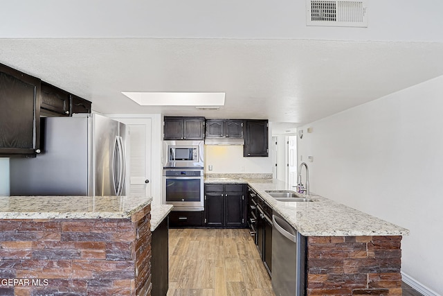 3400 Buffalo Soldier Cir, El Paso, TX 79936 - kitchen featuring stainless steel appliances, a sink, a peninsula, light wood-style floors, and light stone countertops