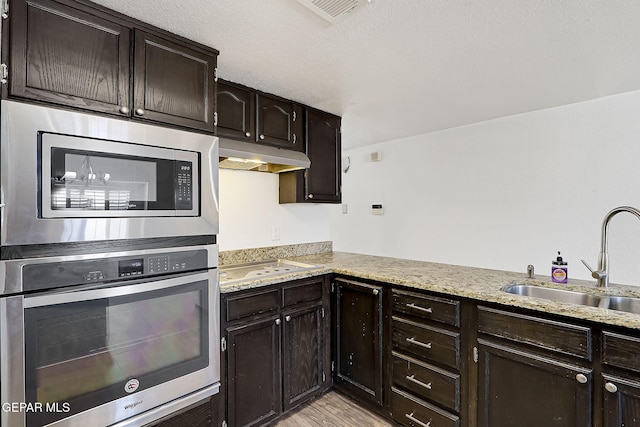 3400 Buffalo Soldier Cir, El Paso, TX 79936 - kitchen featuring appliances with stainless steel finishes, a sink, under cabinet range hood, dark brown cabinetry, and light wood-style floors
