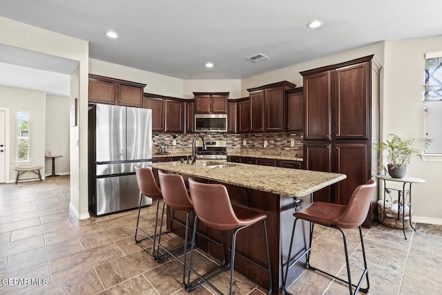 5525 Valley Cedar Dr, El Paso, TX 79932 - kitchen featuring appliances with stainless steel finishes, a sink, an island with sink, tasteful backsplash, and light stone countertops