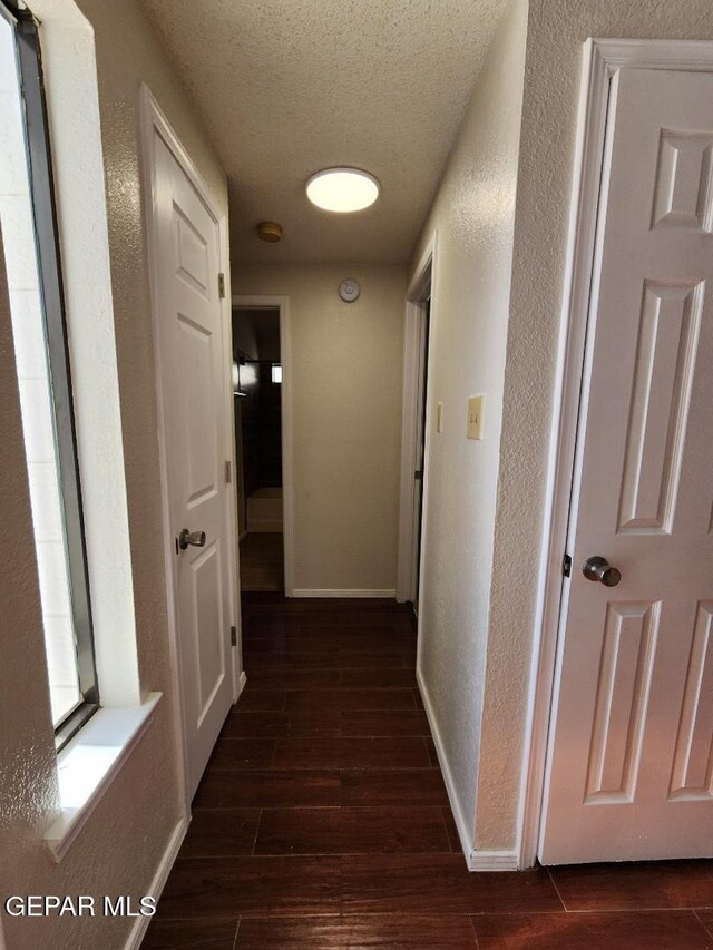 corridor featuring a textured wall, dark wood-style floors, a textured ceiling, and baseboards