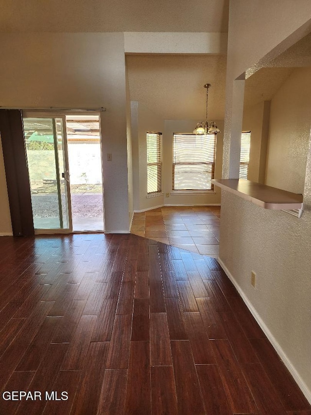 spare room featuring a chandelier, dark wood finished floors, and baseboards