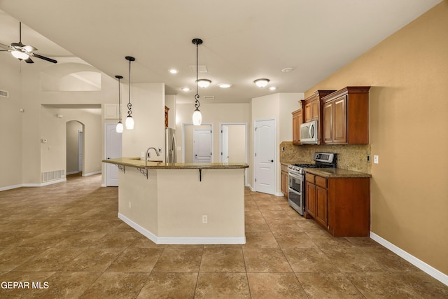 14117 Rainbow Point Dr, El Paso, TX 79938 - kitchen featuring appliances with stainless steel finishes, a breakfast bar area, brown cabinetry, ceiling fan, and tasteful backsplash