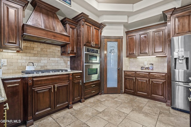 3089 Snowy Point Dr, El Paso, TX 79938 - kitchen with stainless steel appliances, custom range hood, decorative backsplash, light stone countertops, and dark brown cabinets