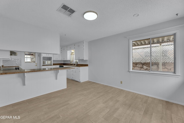 10125 Castletown Dr, El Paso, TX 79925 - kitchen featuring light wood-style flooring, a sink, white cabinets, a textured ceiling, and a breakfast bar