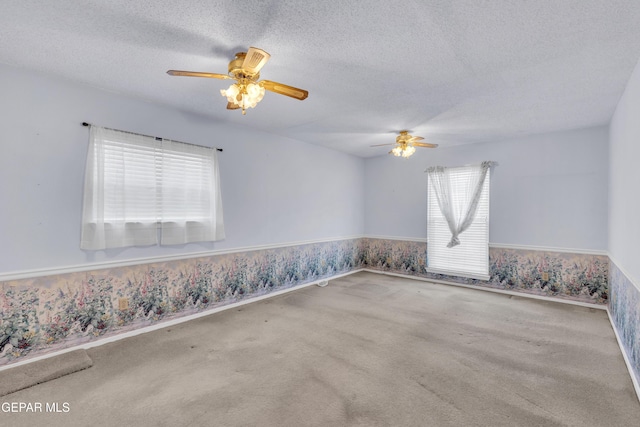 carpeted empty room featuring ceiling fan, wainscoting, a textured ceiling, and wallpapered walls
