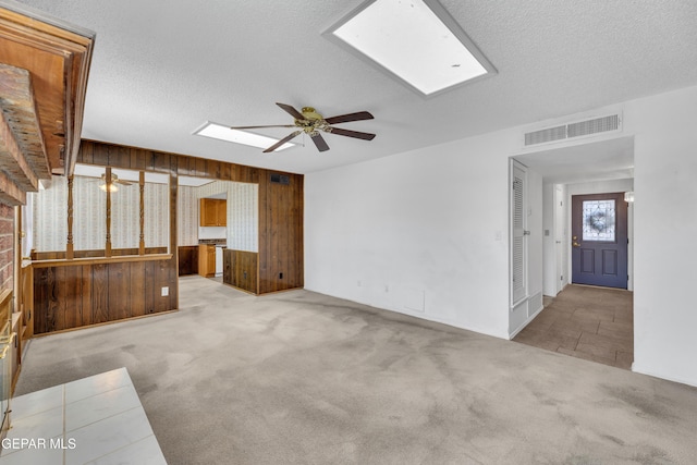 unfurnished living room with a ceiling fan, wood walls, carpet flooring, a skylight, and a textured ceiling