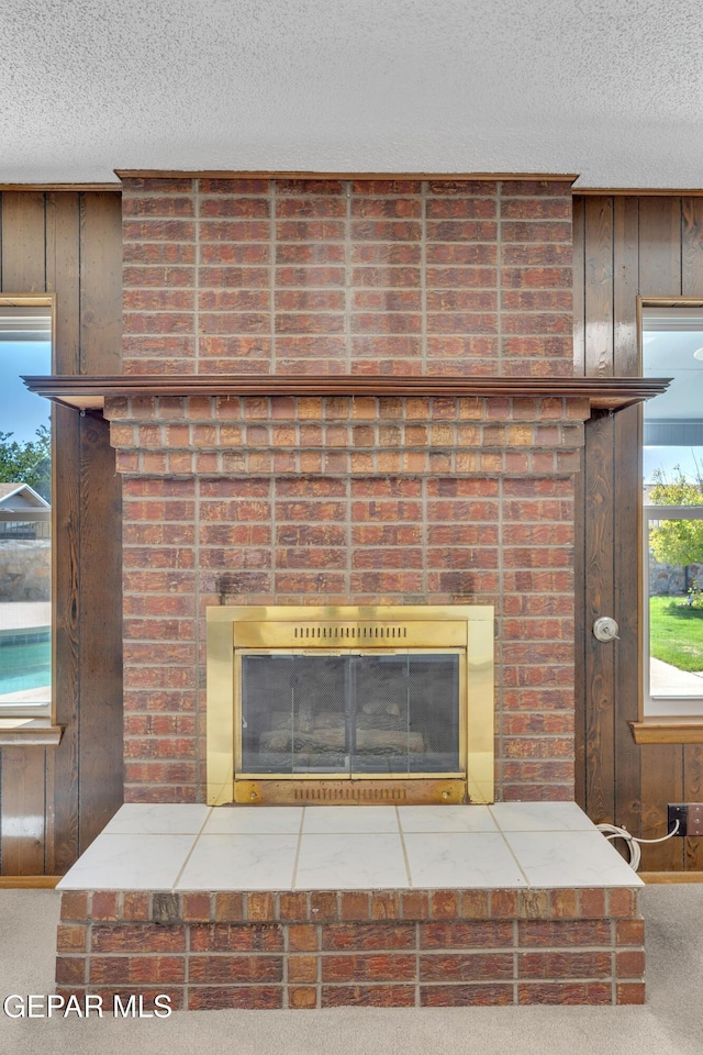 detailed view of a fireplace, a textured ceiling, wooden walls, and carpet flooring