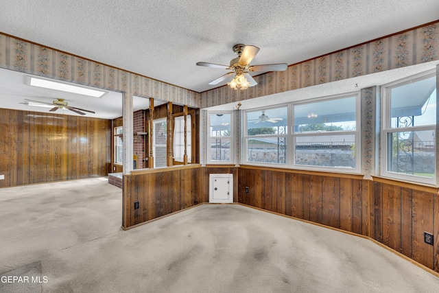 spare room with healthy amount of natural light, ceiling fan, wood walls, a textured ceiling, and carpet flooring