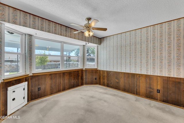 unfurnished room with wainscoting, wooden walls, a textured ceiling, ceiling fan, and carpet flooring