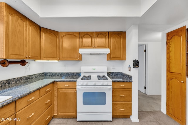 kitchen with white gas range, under cabinet range hood, brown cabinets, and light tile patterned floors