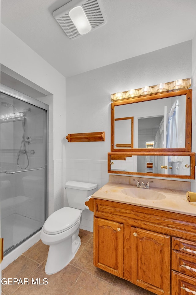 bathroom featuring a shower stall, toilet, vanity, tile walls, and tile patterned floors