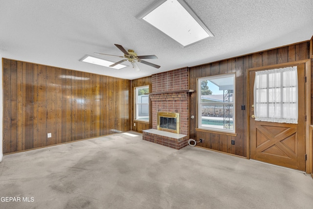 unfurnished living room with wooden walls, a textured ceiling, ceiling fan, a skylight, and a fireplace