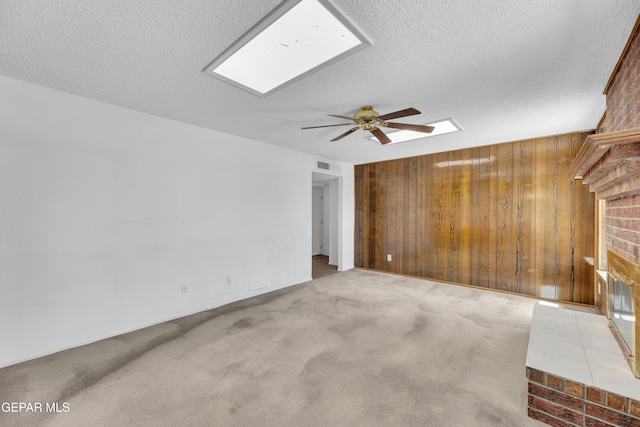 unfurnished living room featuring wooden walls, a fireplace, a ceiling fan, a skylight, and a textured ceiling
