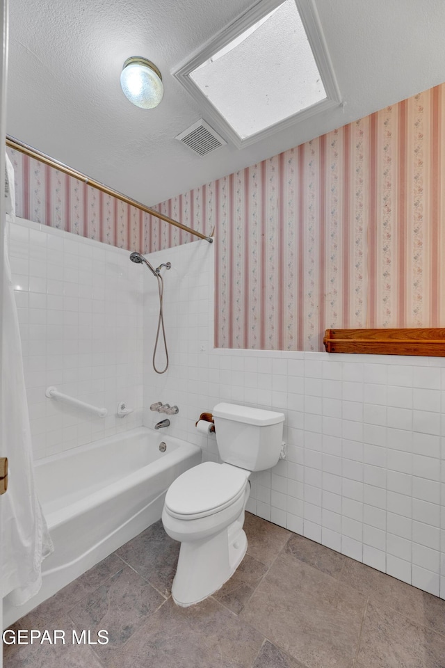 bathroom featuring toilet, shower / tub combo with curtain, tile patterned floors, wainscoting, and tile walls