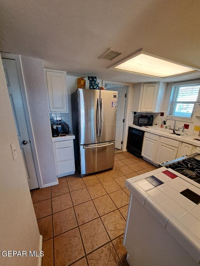 kitchen featuring black appliances, tile counters, white cabinets, light tile patterned floors, and a textured ceiling