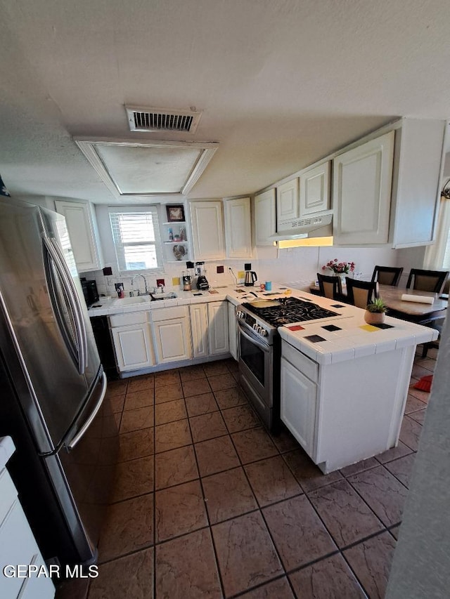 kitchen with stainless steel appliances, under cabinet range hood, tile counters, a sink, and white cabinetry