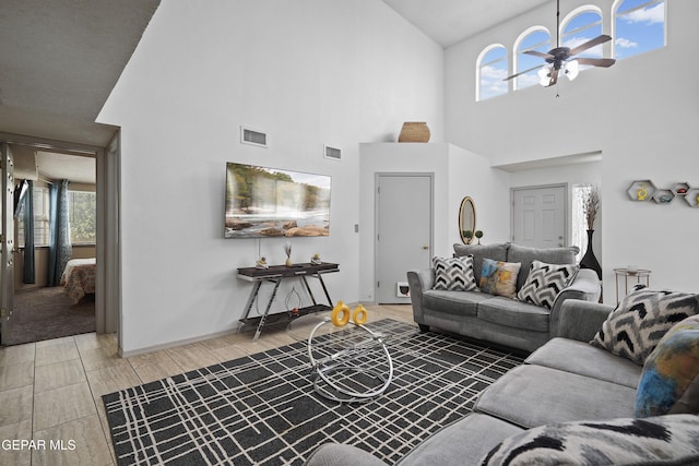 living room with a ceiling fan, a high ceiling, healthy amount of natural light, light wood-type flooring, and baseboards