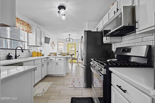 kitchen featuring appliances with stainless steel finishes, a sink, white cabinetry, a peninsula, and light countertops