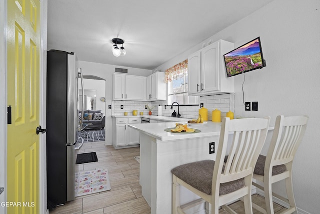 kitchen with freestanding refrigerator, a peninsula, white cabinetry, a breakfast bar, and decorative backsplash