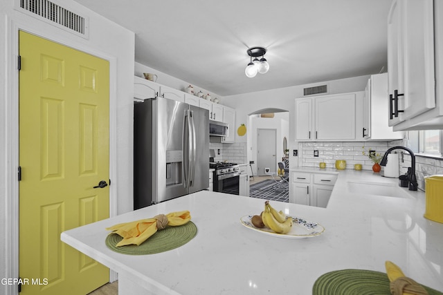 kitchen featuring stainless steel appliances, a sink, tasteful backsplash, white cabinets, and light countertops