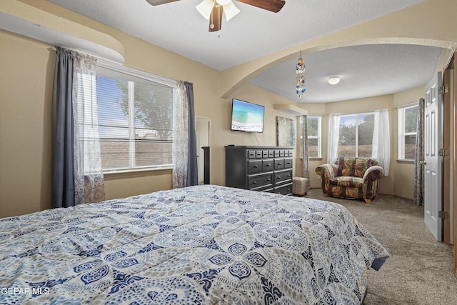 carpeted bedroom featuring arched walkways, a textured ceiling, and ceiling fan