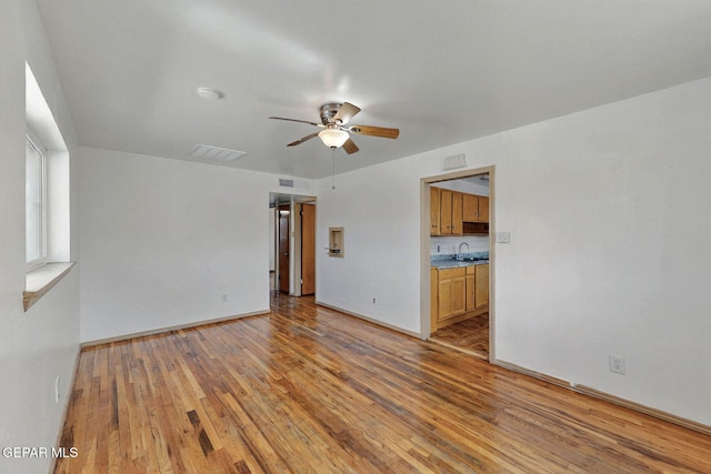 unfurnished living room featuring a ceiling fan, light wood finished floors, a sink, and baseboards