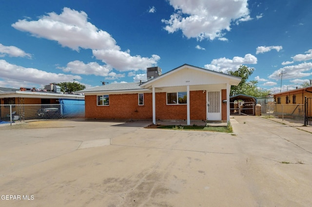 view of front facade with fence, brick siding, a carport, and central AC