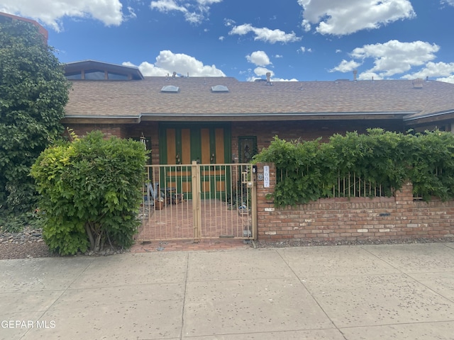 view of front of home with a fenced front yard, roof with shingles, a gate, and brick siding