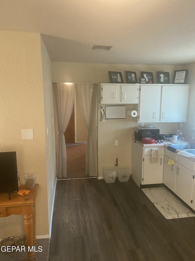 kitchen with white cabinets, a sink, wood finished floors, a textured wall, and baseboards