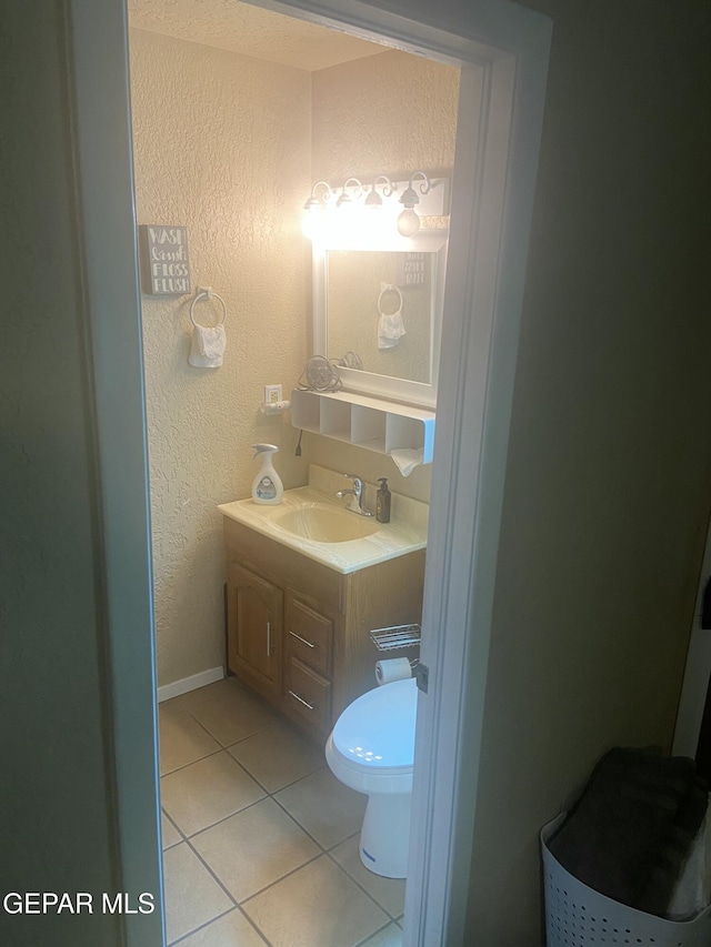bathroom featuring tile patterned flooring, a textured wall, vanity, and toilet