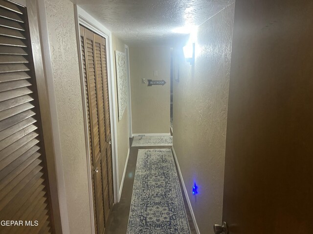 hall with a textured wall, baseboards, and a textured ceiling