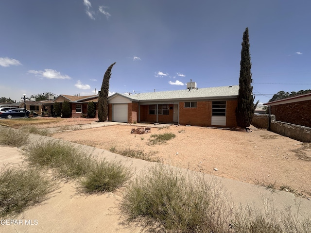 ranch-style home featuring an attached garage, dirt driveway, brick siding, and fence