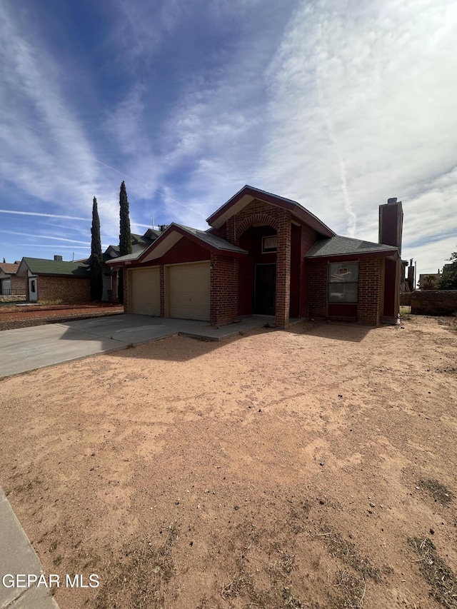view of front of house with an attached garage, brick siding, driveway, and a chimney