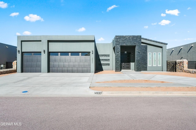 contemporary house with an attached garage, driveway, stone siding, and stucco siding