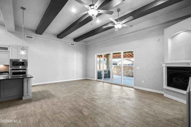 unfurnished living room featuring baseboards, ceiling fan, beam ceiling, a fireplace, and wood finished floors