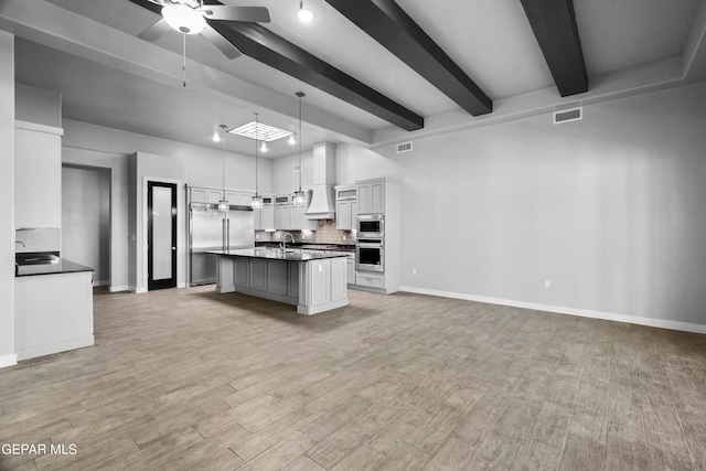 kitchen with dark countertops, custom range hood, built in appliances, a sink, and beamed ceiling