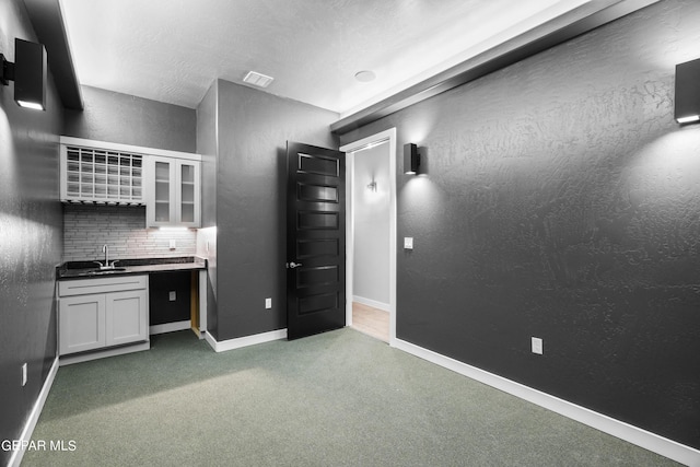 kitchen with baseboards, a sink, decorative backsplash, glass insert cabinets, and white cabinets